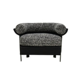 The Elias Armchair featuring a sculptural curved silhouette, upholstered in soft woven fabric with a contrasting genuine leather outer shell, styled in a modern living room setting.