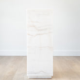 Modern marble plinth with a polished white stone finish, styled as a pedestal for sculpture in a minimalist living room.