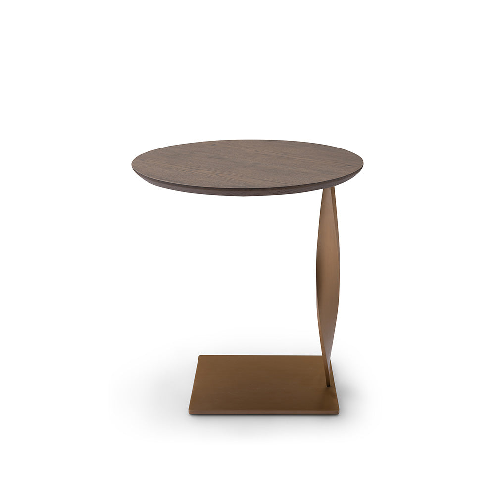 Close-up of a modern side table featuring an elm veneer top and a sculptural twisted brushed brass base, styled in a contemporary living room.