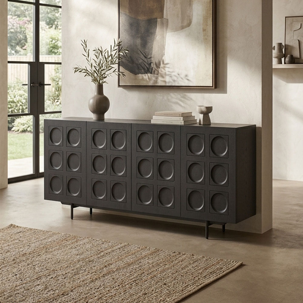A dark charcoal gray sideboard or credenza with a grid pattern of circular recessed details, styled in a modern living room setting with a vase, books, and a rug.