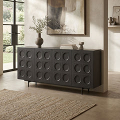 A dark charcoal gray sideboard or credenza with a grid pattern of circular recessed details, styled in a modern living room setting with a vase, books, and a rug.