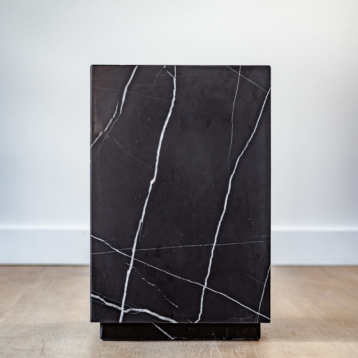 Tall black marble display plinth with polished finish and subtle white veining, placed in a luxury gallery setting.