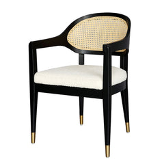 Ylva Dining Chair featuring black rubberwood frame, natural rattan back, white cotton-polyester bouclé seat with silk underlay, foam padding, and brass gold-capped legs for classic comfort and elegance.