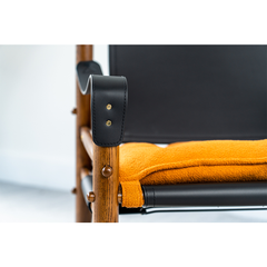 Designer lounge chair with ash wood frame, black leather seat, and vibrant orange cushion for contemporary living rooms