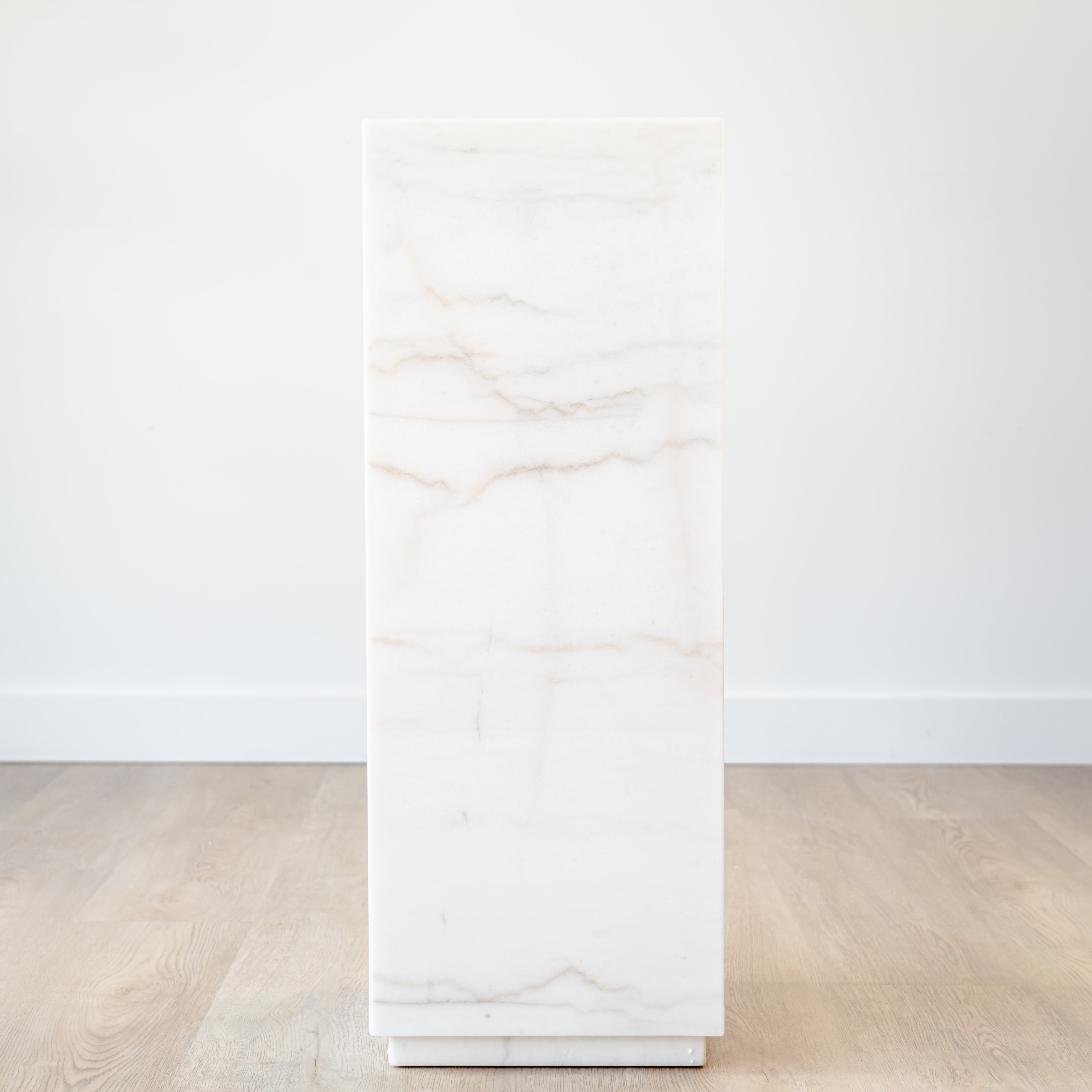 Modern marble plinth with a polished white stone finish, styled as a pedestal for sculpture in a minimalist living room.