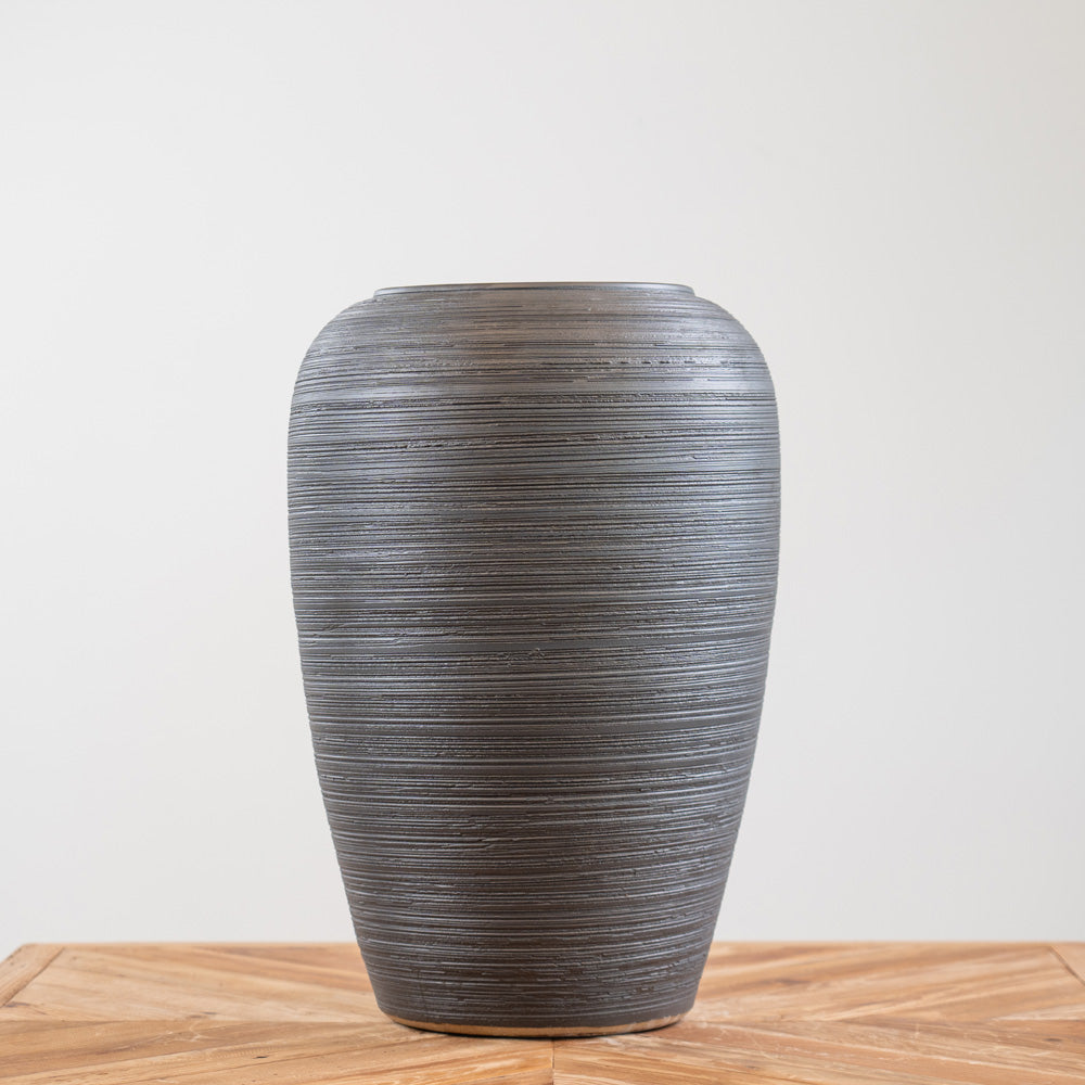 Tall black ceramic planter with textured lines, weather-resistant design, and drainage hole, suitable for indoor and outdoor use.