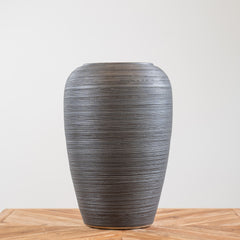 Tall black ceramic planter with textured lines, weather-resistant design, and drainage hole, suitable for indoor and outdoor use.
